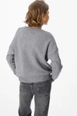 Sweater de punto negro con diseño de trenzas verticales en el frente y cuello redondo. Presenta un corte holgado con puños y ruedo acanalados.