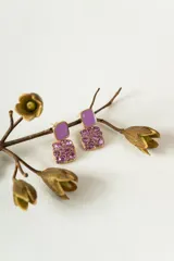 Aros colgantes con diseño cuadrado, compuestos por una pieza superior esmaltada en color lila y una pieza inferior decorada con cristales facetados en tonos rosados y violetas sobre base dorada.