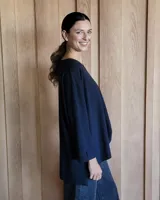 Remerón de corte oversize color beige, con cuello redondo, mangas largas y diseño asimétrico con la parte trasera más larga que la delantera y aberturas laterales en el ruedo.
