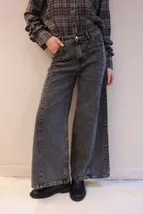 Pantalón de jean color gris oscuro, de corte wide leg con costuras verticales decorativas en el frente. Presenta cintura alta con cierre de botón y cremallera.