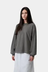 Remera de manga larga gris oscuro de corte holgado, confeccionada en algodón orgánico con efecto desteñido. Presenta cuello redondo y una pequeña etiqueta cuadrada en el dobladillo inferior.