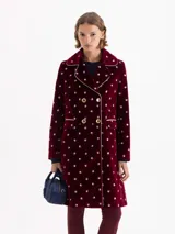 Tapado de velvet color bordó con estampado floral en blanco, forrado en jacquard beige. Presenta cuello tipo Peter Pan con solapa redondeada y vivo en contraste que enmarca cuello, cartera y bolsillos. El acceso es mediante cruce diagonal con cuatro broches dorados. Lleva recortes en cintura, costadillos y pinzas que estructuran la silueta, junto con hombreras que aportan porte. Largo por debajo de la rodilla.