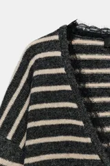 Jersey de punto a rayas horizontales en color gris y beige, con escote en pico profundo y detalle de encaje negro en el borde. Presenta mangas largas y corte ligeramente cropped.