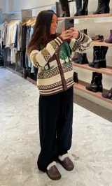 Cardigan de punto con diseño artesanal de paisaje boscoso, cuello polo y cierre frontal con botones metálicos. Presenta un patrón de franjas horizontales en tonos marrón, crema y detalles en beige, con mangas largas y puños acanalados.
