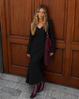 Vestido midi de color negro, confeccionado en tejido plisado con escote en V y mangas largas acampanadas.