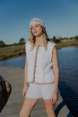 Conjunto tejido de algodón color blanco, compuesto por un chaleco con botones y shorts con cintura elastizada. El chaleco tiene cuello redondo y terminaciones en punto ocre. El short tiene terminaciones en punto ocre.