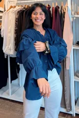 Camisa de pana fina color azul, con diseño de volados en los hombros y mangas largas abullonadas con puños elásticos. Presenta cierre frontal con botones y cuello con detalle de volado.