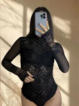 Body de encaje y microtul color negro, con mangas largas, cuello alto y diseño entallado que combina transparencias.