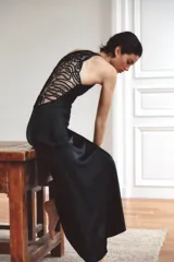 Vestido largo de satén con cuello halter ajustable y hombros descubiertos. Presenta un diseño elegante con espalda detallada en tejido con relieve y bordados perforados. Incluye cierre lateral con cremallera oculta.