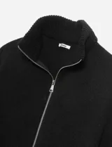 Poncho tejido color bordó con cuello alto y cierre frontal completo. Presenta mangas cortas con terminación en puño acanalado y un diseño holgado.