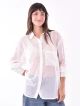 Camisa blanca traslúcida con rayas verticales doradas, de corte holgado, manga 3/4 y bolsillo en el pecho.
