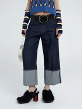 Pantalón de jean azul oscuro de corte ancho, con tiro medio y un marcado doblez en el bajo que deja ver el tono más claro del denim. Presenta costuras en contraste y un diseño de pierna recta.