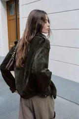 Cazadora de piel ante color verde oscuro, con cuello solapa, manga larga con trabillas en los hombros, bolsillos delanteros de plastrón con solapa y botones a presión, bajo elástico y cierre frontal con cremallera.