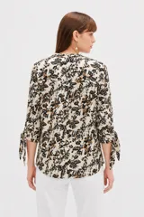 Blusa estampada de viscosa con diseño abstracto en tonos beige, negro y marrón, escote en V con cuello mao y mangas tres cuartos con detalles de lazos en los puños.