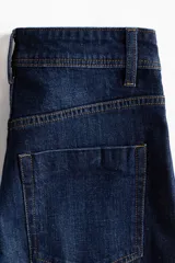 Jean ancho de tiro alto confeccionado en denim de algodón con ligero stretch, de color azul oscuro con efecto deslavado y pliegues frontales.
