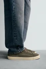 Zapatilla de cordones confeccionada en piel con acabado de serraje. Presenta un diseño liso con detalle de color a contraste en el talón y suela plana de goma a contraste.