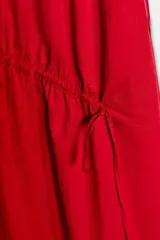 Vestido midi de color rojo confeccionado en tejido de nylon. Presenta un diseño sin mangas con cuello redondo y detalles de frunces horizontales con lazadas laterales ajustables. Cuenta con un cierre en la espalda mediante abertura y botón.