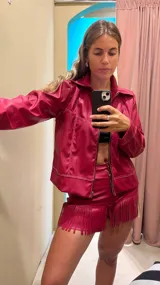 Campera corta color fucsia, con cuello camisero, cierre frontal con cremallera y costuras decorativas en hilo blanco.