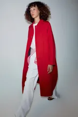 Trench largo color rojo de la línea ZW Collection de Zara, con cuello solapa, manga larga y bolsillos laterales ocultos. Presenta un diseño con forro interior a contraste y cierre frontal con botones a presión.