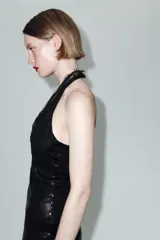 Vestido corto de lentejuelas negras con cuello halter y escote en pico profundo. Presenta detalles de encaje en el escote y espalda descubierta con cierre de botones en el cuello.