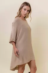 Maxi sweater tejido color beige con efecto metalizado sutil, silueta amplia, mangas tipo murciélago y largo asimétrico (más corto adelante y más largo atrás).