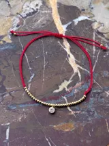 Pulsera roja ajustable con cierre de nudo macramé, cuentas de 2mm en oro laminado 14k (Goldfilled) y punto de luz engarzado en oro laminado.