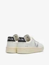 Championes Veja modelo V-90, color blanco con detalles en plateado y negro. Presentan el logo de la marca en el lateral, puntera perforada y suela de goma en tono crema.