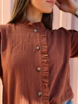 Camisa de manga larga color marrón chocolate, con cuello alto y detalles de volados a lo largo de la botonadura frontal.