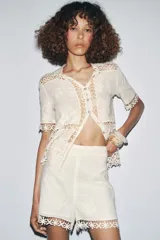 Blusa de algodón color crudo con detalle de bordados y crochet. Cuello redondo, manga corta y cierre frontal con botones.