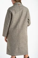 Tapado largo de corte oversize en color beige, con solapas clásicas y cierre frontal con botones. Presenta un diseño minimalista y elegante, ideal para un look sofisticado.