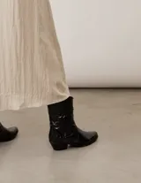 Bota corta de cuero acharolado negro con diseño estilo texano, punta afinada, taco bajo y costuras decorativas en la caña.