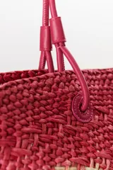 Bolso tipo shopper de paja trenzada color rosa con detalles en beige. Tiene doble asa de cuero sintético color fucsia.