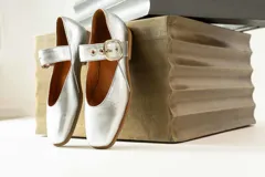 Zapato tipo Mary Jane plateado con correa sobre el empeine y hebilla metálica.