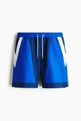 Short de baño tipo boxer, confeccionado en nylon, con diseño en bloques de color azul, azul marino y blanco. Presenta cintura elástica con cordón ajustable blanco, bolsillos laterales y aberturas en el dobladillo.