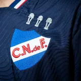 Camiseta de fútbol Umbro del Club Nacional de Football, modelo Away 2. Diseño en azul marino con tramado sutil de líneas onduladas, detalles en rojo, blanco y azul en el cuello y los puños. Incluye el logo de Umbro, el escudo del club y el sponsor Antel en el pecho.