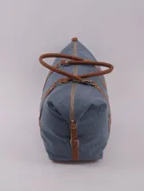 Bolso de viaje tipo duffle, confeccionado en cuero natural color azul con textura, con detalles de correas y asas en cuero color suela. Cuenta con cierre superior, bolsillo interior con cierre y compartimento para celular.