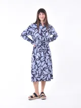 Vestido camisero midi de manga larga, con cuello y botones frontales, ajustado a la cintura con un lazo. Presenta un estampado abstracto en tonos azul claro y azul oscuro/negro.