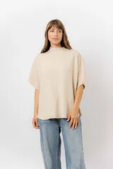 Sweater de tejido de punto en color beige, con cuello semi alto y mangas cortas amplias. Presenta una silueta relajada y corte holgado con caída fluida.