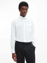 Camisa de corte relajado confeccionada en popelina de algodón con elastano. Presenta cuello clásico, cierre frontal con botones, mangas largas con puños abotonados y un bolsillo frontal con solapa en el pecho.