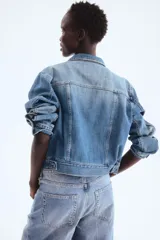 Campera de denim de algodón rígido, color azul, con cuello clásico y cierre frontal de botones metálicos. Cuenta con bolsillos superiores con solapa y botón, bolsillos laterales insertados y puños abotonados.