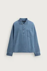 Camisa polo de denim celeste con corte relaxed fit, cuello solapa, cierre frontal parcial con botones, manga larga con puños abotonados y un bolsillo de parche en el pecho.