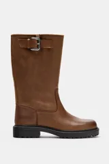 Bota de piel color marrón de caña alta, con detalle de hebilla metálica en la parte superior, efecto desgastado y suela dentada negra.