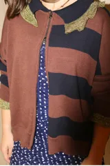 Cardigan de tejido de punto con diseño a rayas horizontales en tonos marrón y azul marino. Presenta cierre frontal con doble cursor, cuello tipo polo con detalles en hilo metalizado dorado y puños con el mismo acabado brillante.