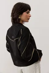 Camisa de manga larga color negro, con cuello camisero, cierre frontal con botones y detalles de ribetes contrastantes en color dorado. Presenta paneles superiores con textura y mangas abullonadas.
