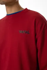 Buzo rojo de jersey doble 100% algodón, con corte levemente boxy y logo frontal serigrafiado en estilo graffiti. Costuras negras visibles y cuello redondo con ribete azul. Hecho en Uruguay.