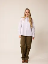 Camisa de manga larga con cuello clásico y cierre frontal de botones, confeccionada en tela de algodón con diseño de rayas verticales finas en color rosado y blanco. Presenta un bolsillo frontal en el pecho con detalle de etiqueta pequeña.