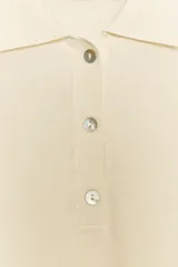 Polo de punto color crema, de manga corta y corte holgado, con cuello polo y tres botones frontales.
