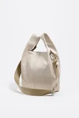 Bolso de mano mediano de piel vacuna, color negro, con estructura blanda y forma de cubo o 'paper bag'. Posee asas de mano cortas y una correa ajustable y extraíble de tela azul marino. El logo de Bimba y Lola está grabado en la parte inferior frontal.