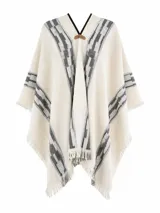 Poncho color beige con diseño de guardas geométricas en tonos grises y negros, detalles de flecos en los bordes y escote en V con aplique de cuero sintético con el logo de la marca.