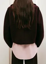 Chaqueta de lana y mezcla sintética color bordó, con cuello amplio, cierre frontal de botones y mangas largas holgadas.